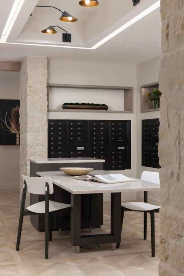 Luxury multifamily mailroom with custom mailboxes, community table seating, stone columns, and modern interior design for residential developments.