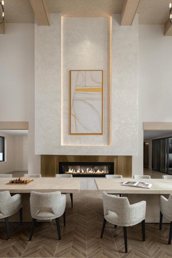 Luxury kitchen and fireplace amenity featuring communal dining table, upholstered seating, architectural fireplace surround, and high-end interior design for multifamily communities.
